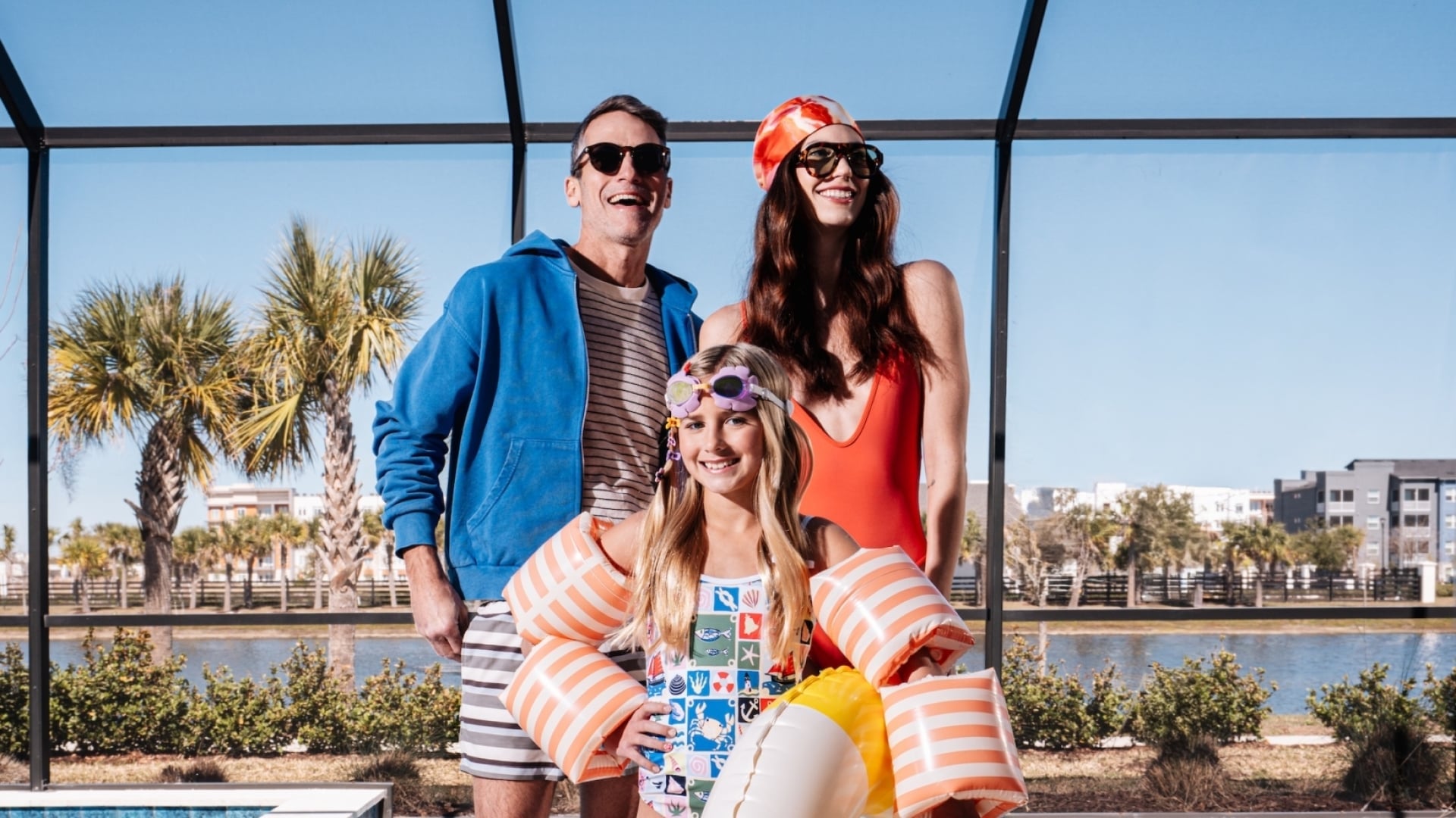A family of three posing by a screened-in private pool with inflatable swim gear and flippers.