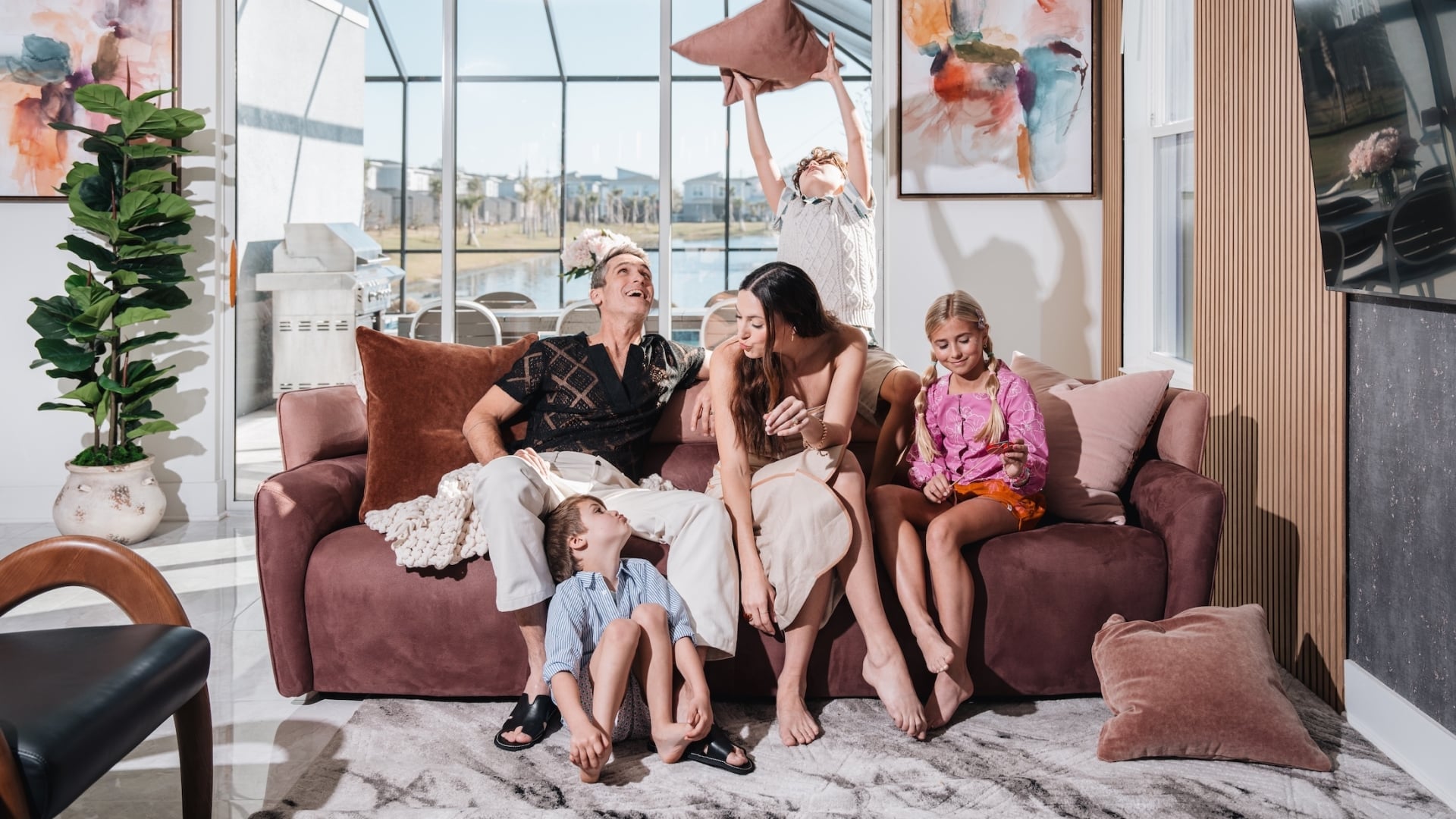 A family relaxing and playing in a modern living room with a large plush sofa and contemporary wood-slat wall.